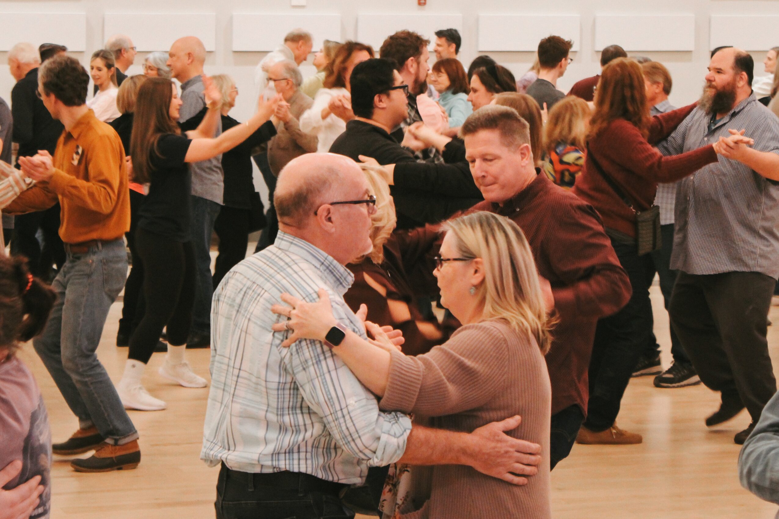Groups of people dance in pairs in a bright indoor room.