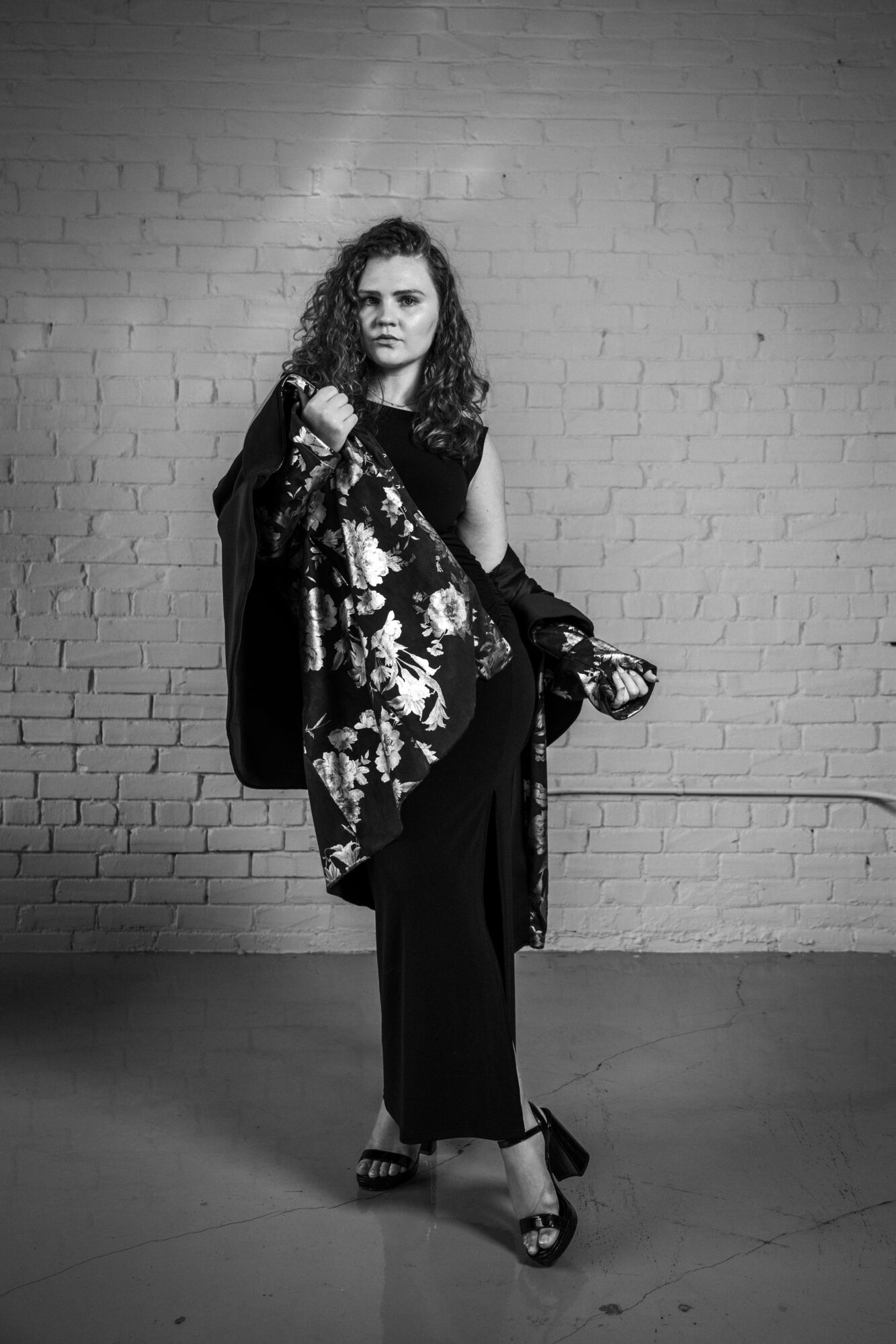 A person in dark clothing holds a patterned garment against a brick wall.