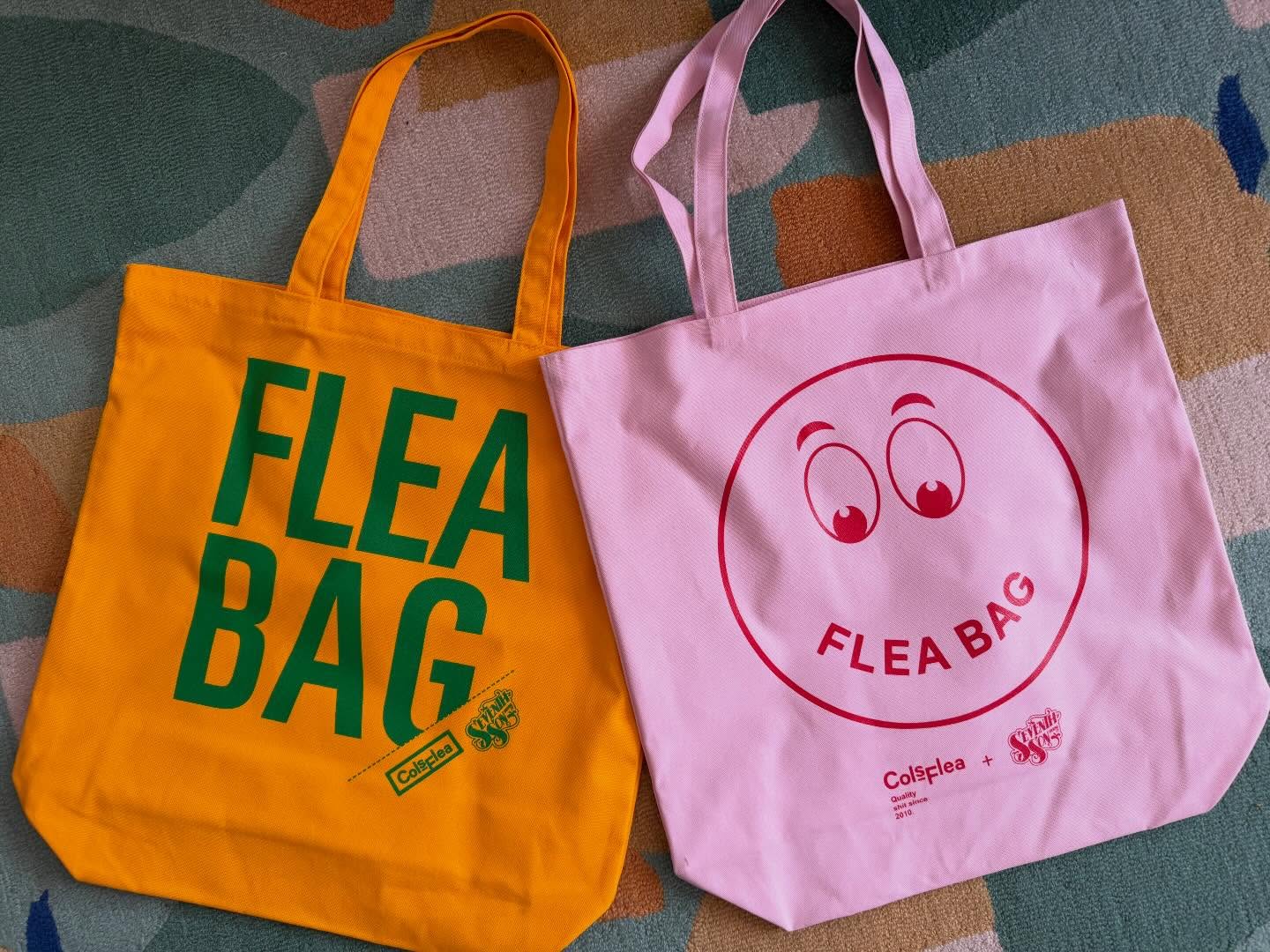 Orange and pink tote bags with green and red flea bag lettering lie on a patterned rug.
