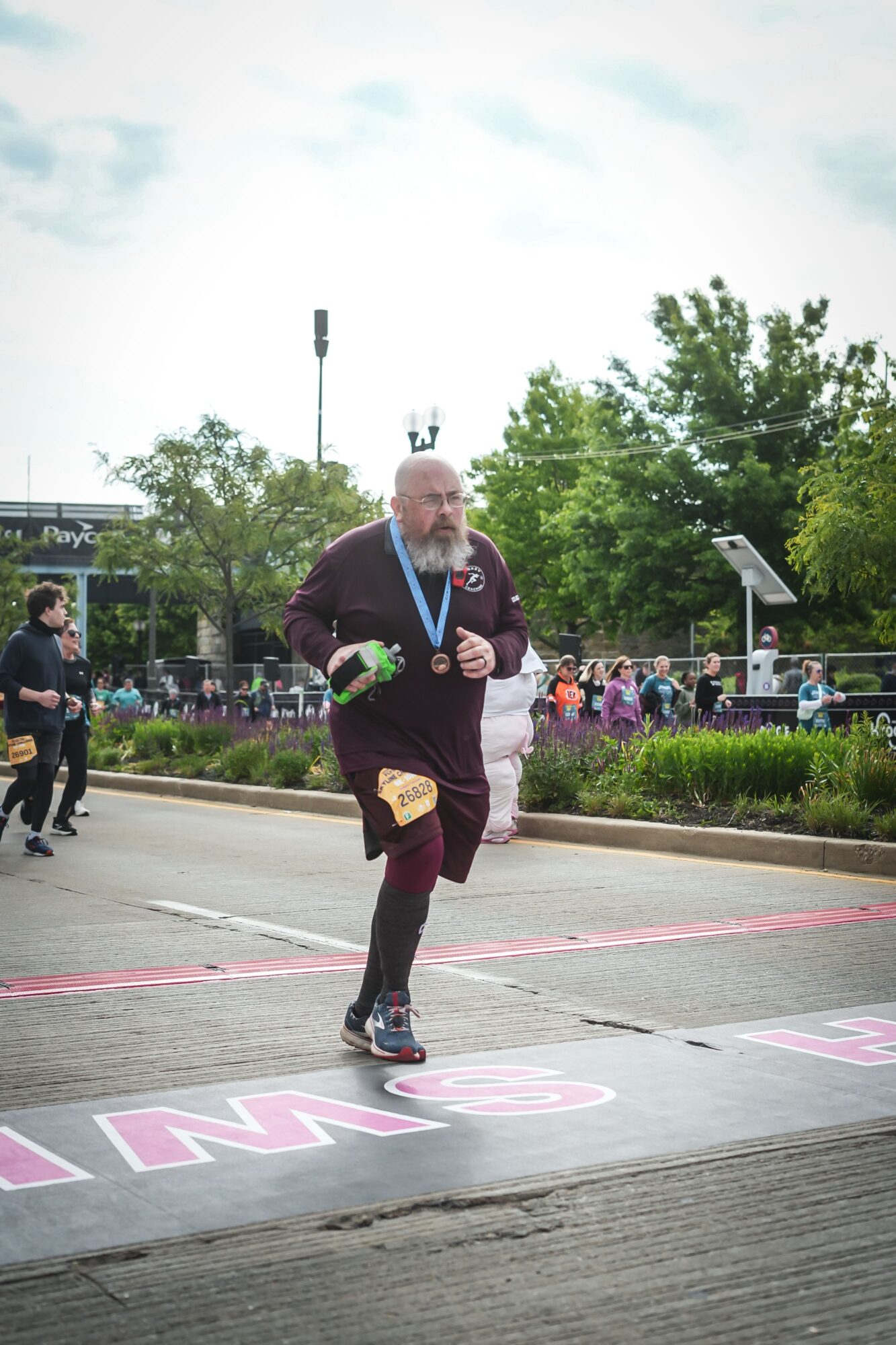 A runner wearing a medal crosses a marked finish line as spectators watch from behind barriers.