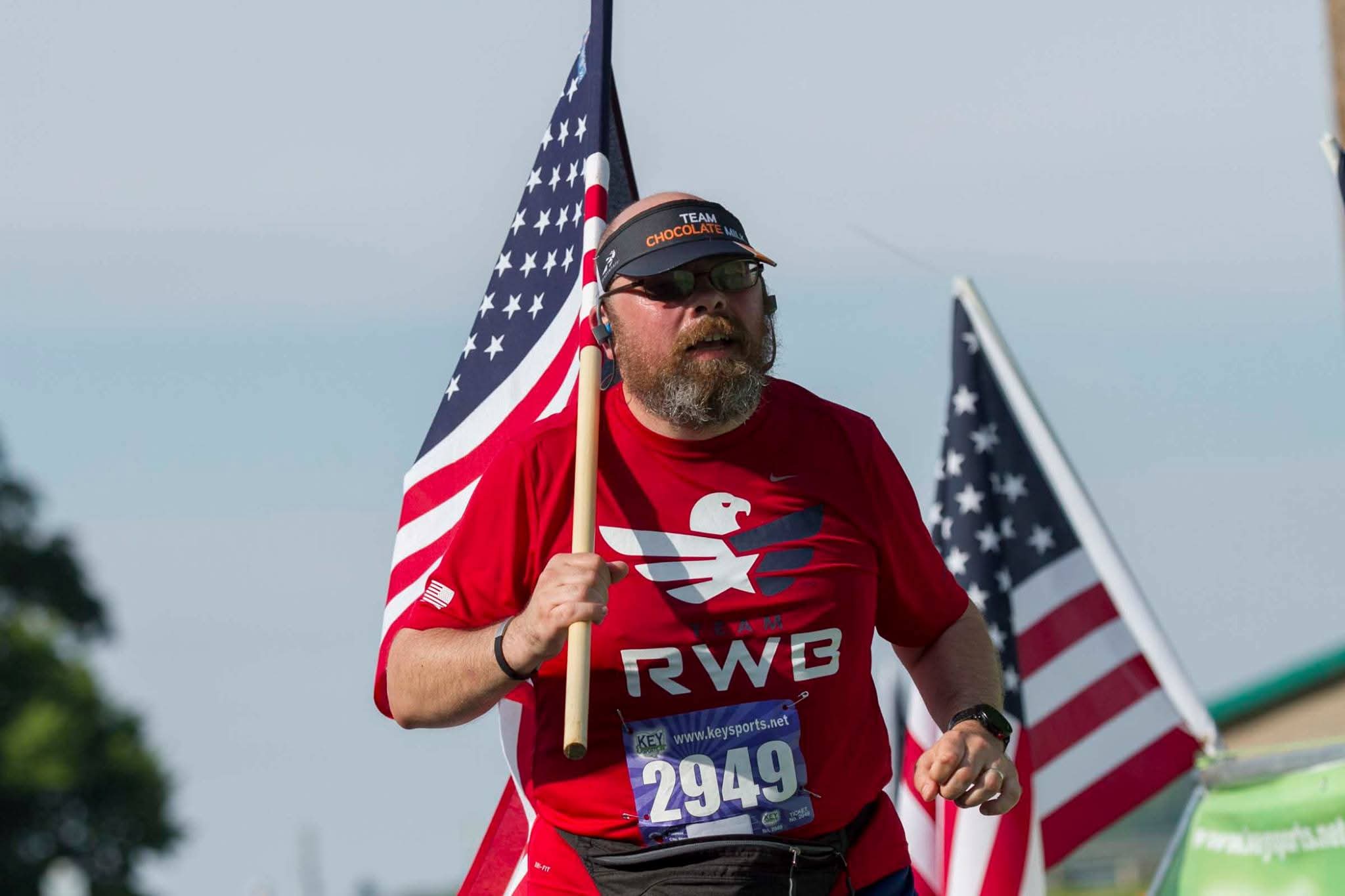 Person in a red shirt holding an American flag, with another flag behind them.