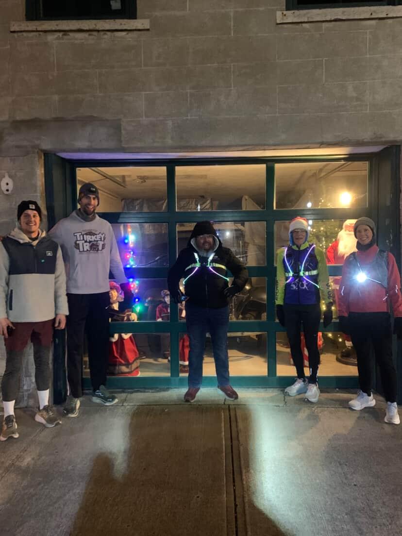 Five people stand outside a glass entrance at night, with colorful lights visible inside.