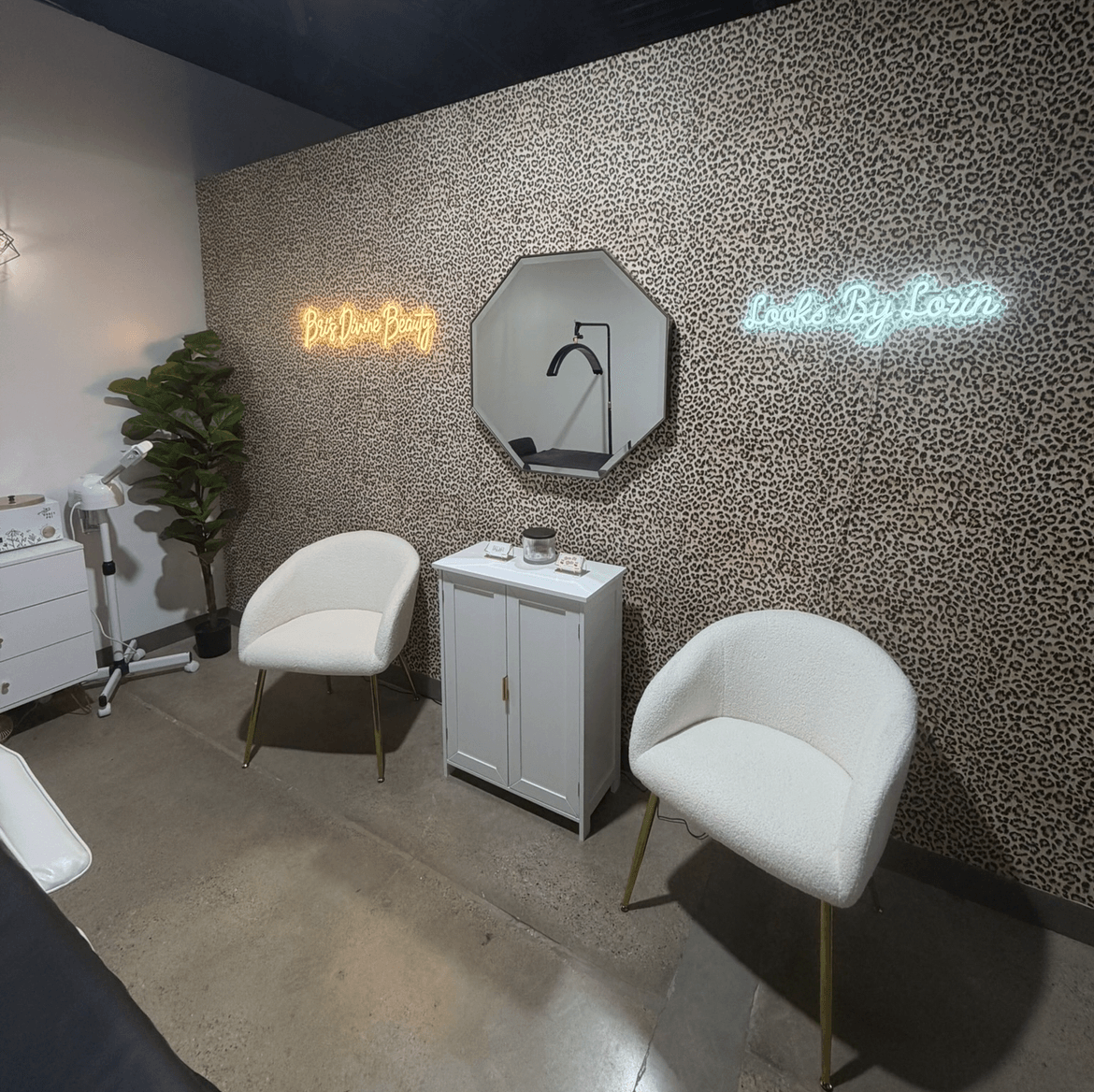 Two white chairs and a cabinet sit beneath a wall mirror and illuminated signs in a patterned room.