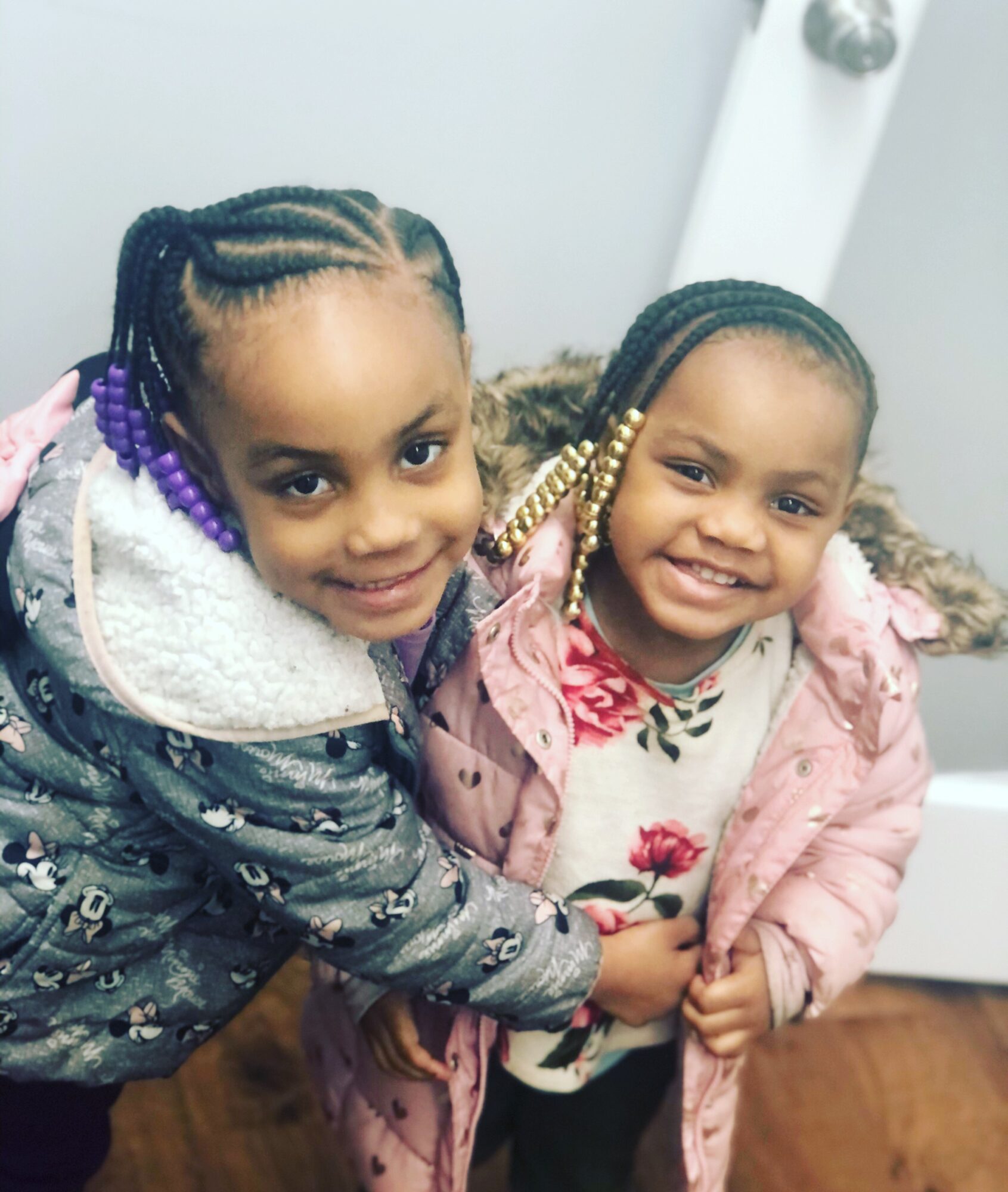 Two children with braided hair stand together in patterned coats.