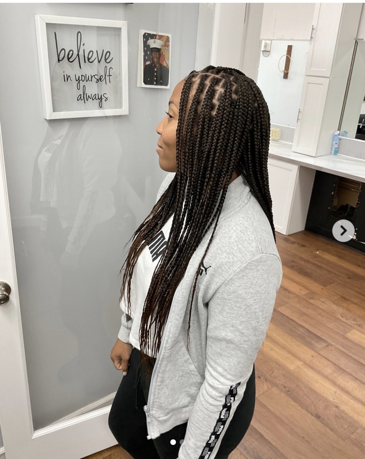 Person with long braids standing beside a glass door with framed wall art in the background.