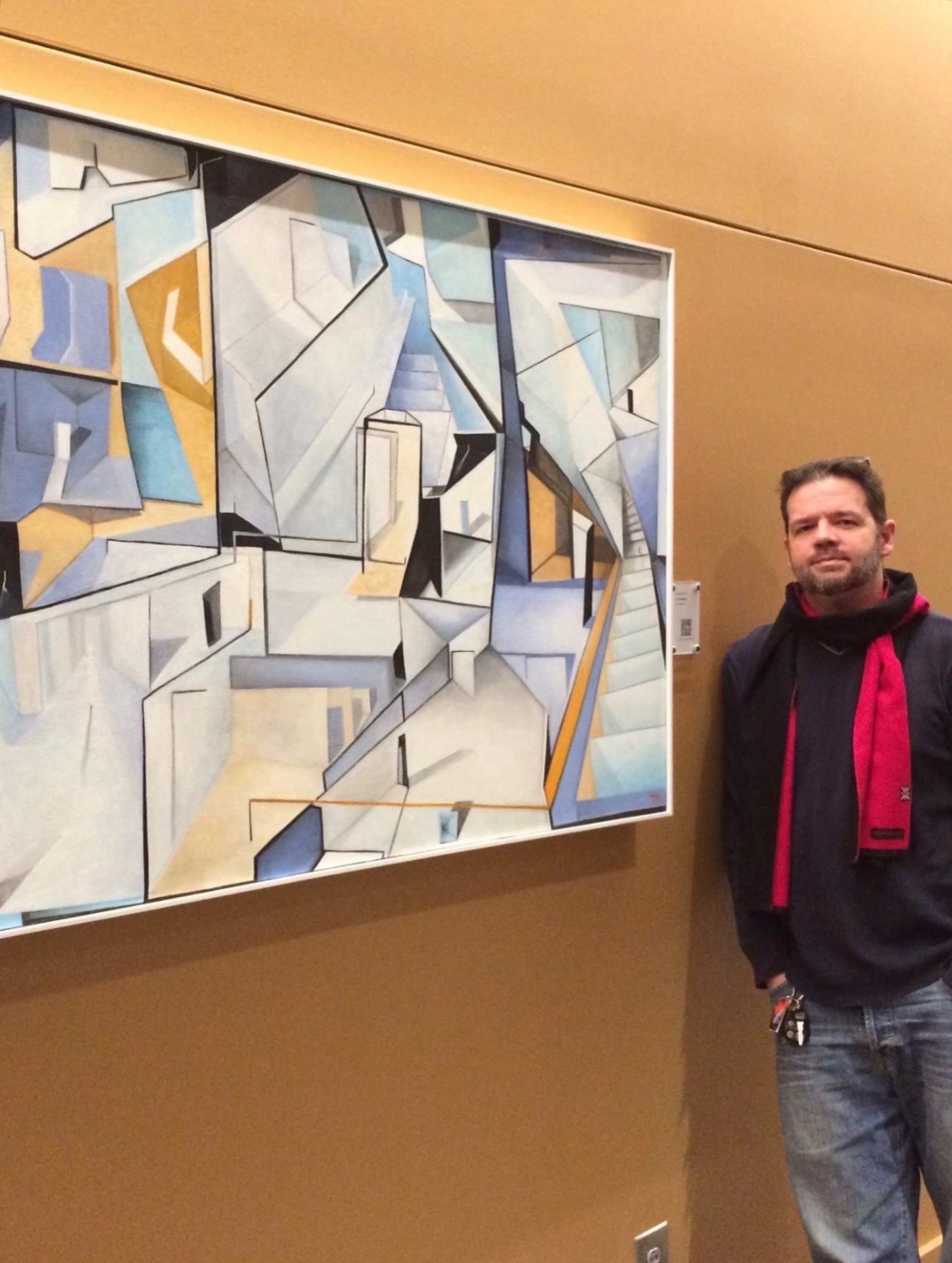 A person stands beside a large geometric abstract painting on a gallery wall.