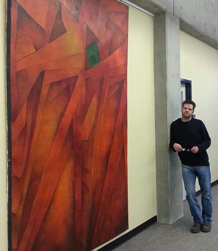A person stands beside a large red and orange abstract painting in a concrete hallway.