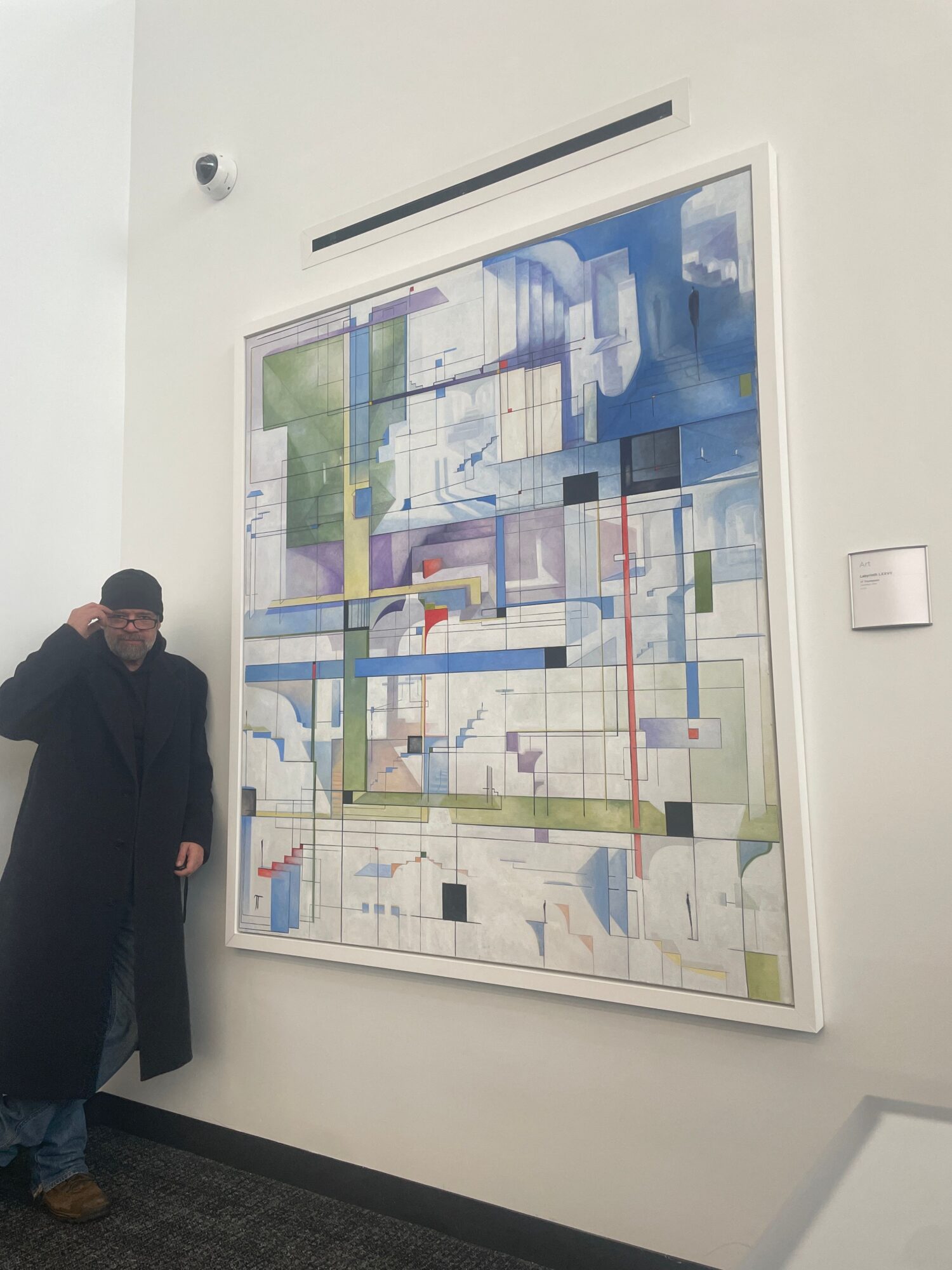 Framed abstract map-like artwork hangs on a wall above a person standing nearby.