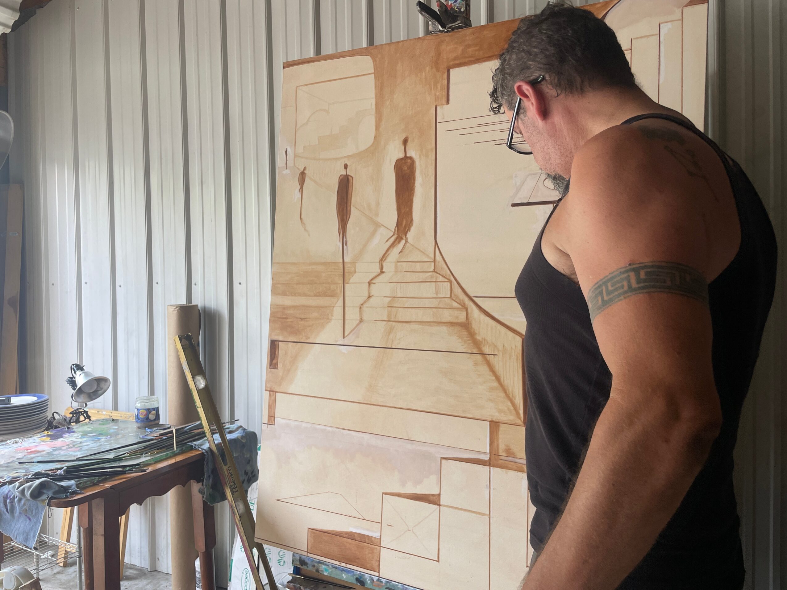 A person stands beside a large wood panel decorated with carved or drawn architectural designs in a workshop.