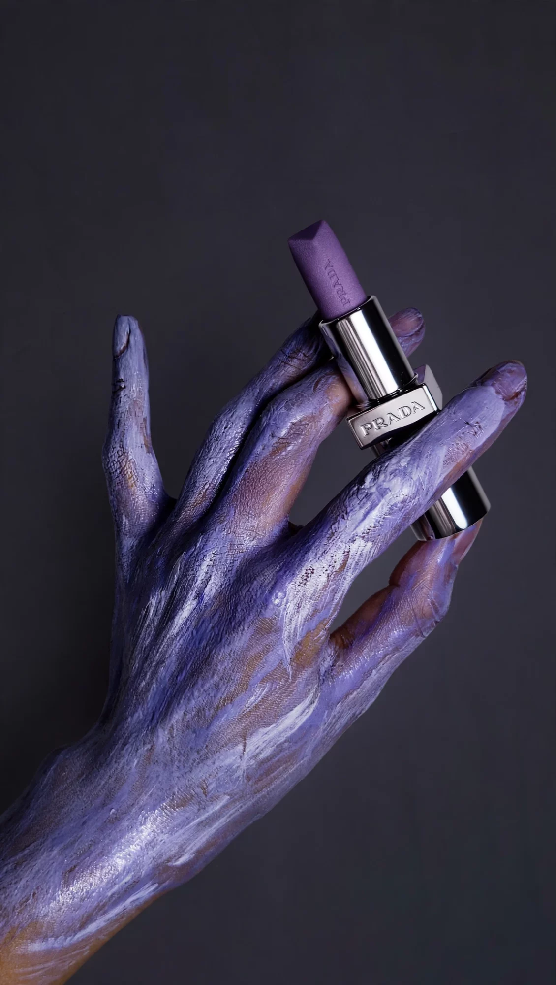 A purple-painted hand holds a lipstick tube with a purple bullet against a dark background.