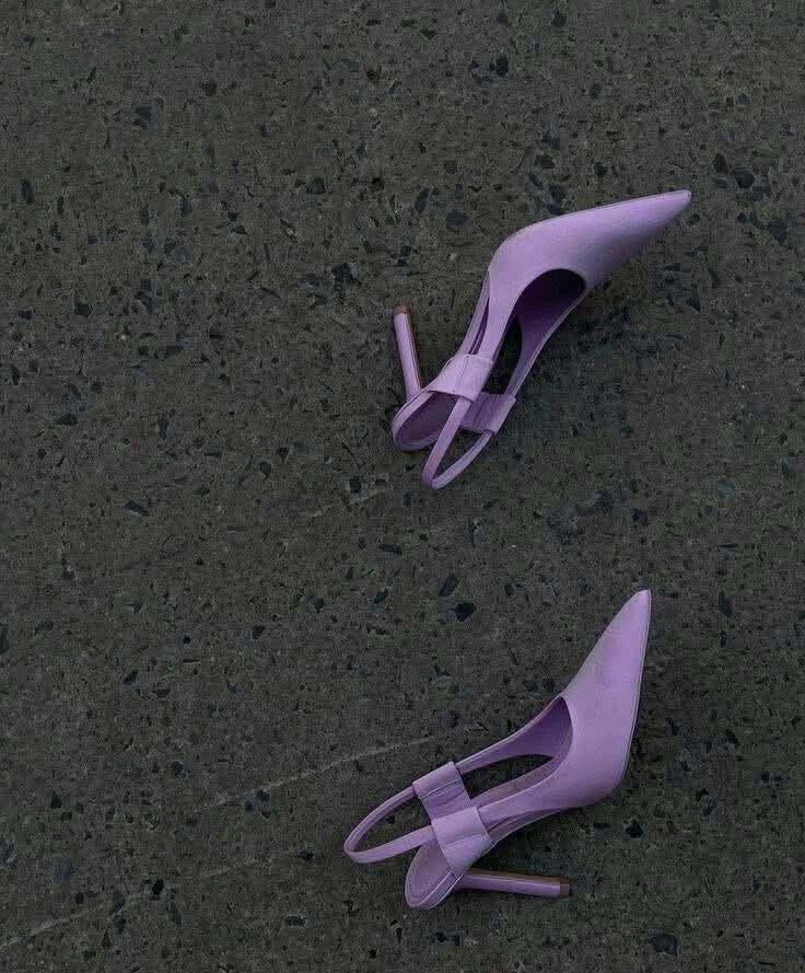 Two purple high-heeled shoes lie apart on a dark speckled floor.